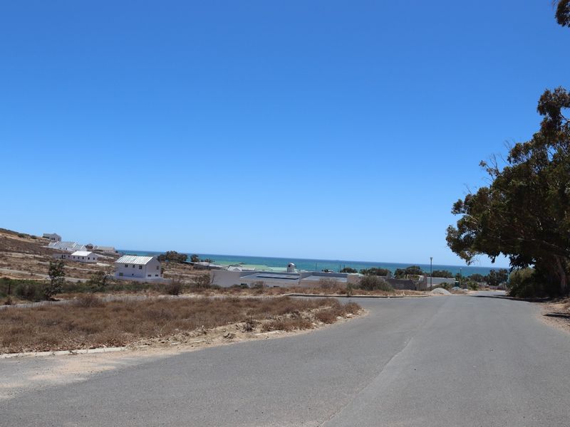 A view of the paved street approach leading towards the coastal residential area with clear ocean views.