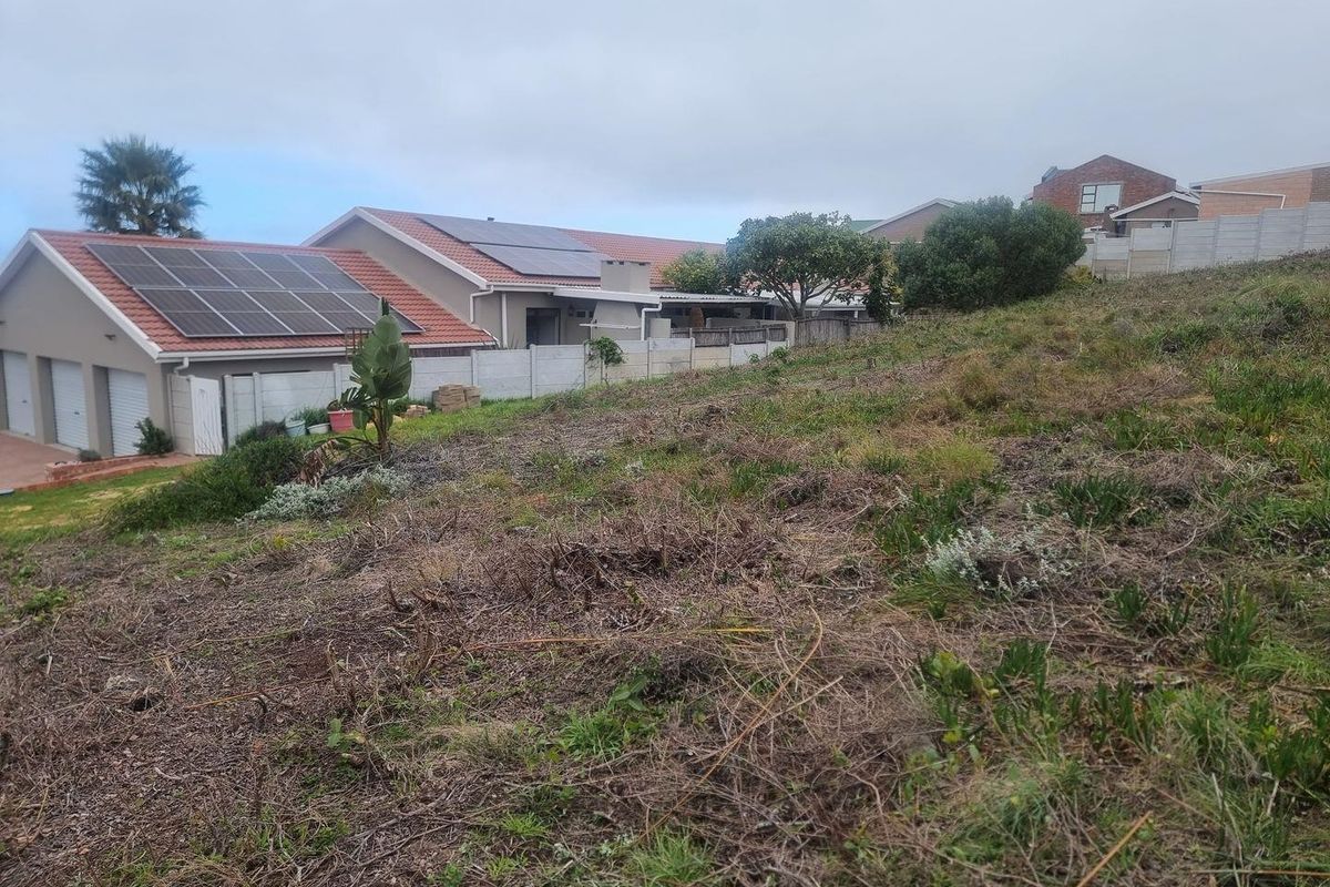 A view of a sloped, undeveloped residential plot adjacent to existing properties with established boundary walls and solar panel installations.