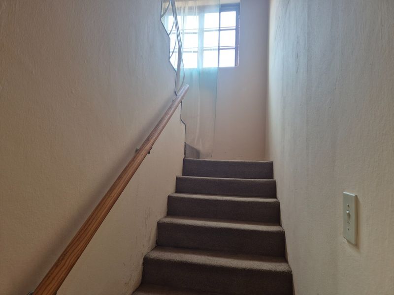 A staircase with a wooden handrail and carpeted steps leading to an upper level, featuring a window for natural light.