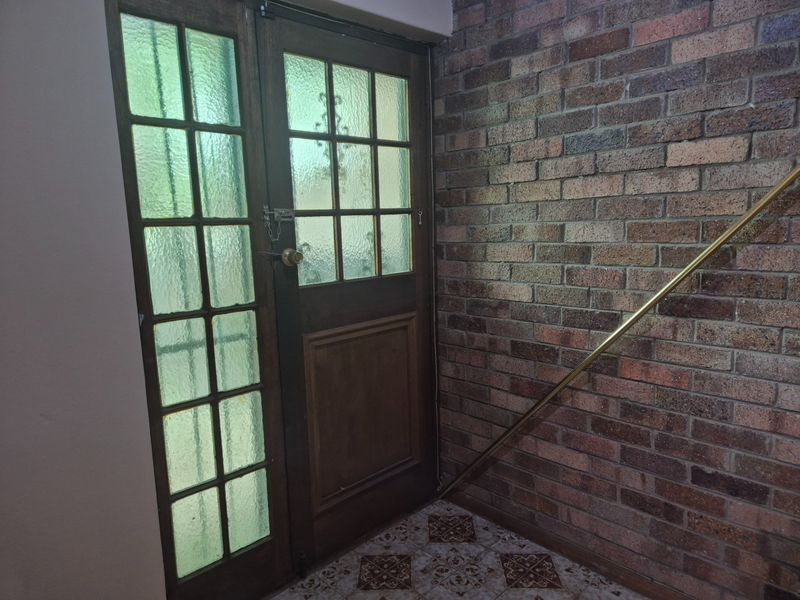 Entrance area featuring a timber-framed glass door, exposed brick wall, and patterned ceramic floor tiles with a brass handrail.