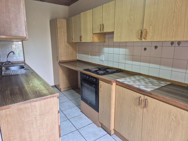 A dated kitchen featuring laminate cabinetry, built-in oven, electric hob, and tiled backsplash, offering a functional layout ready for modernization.