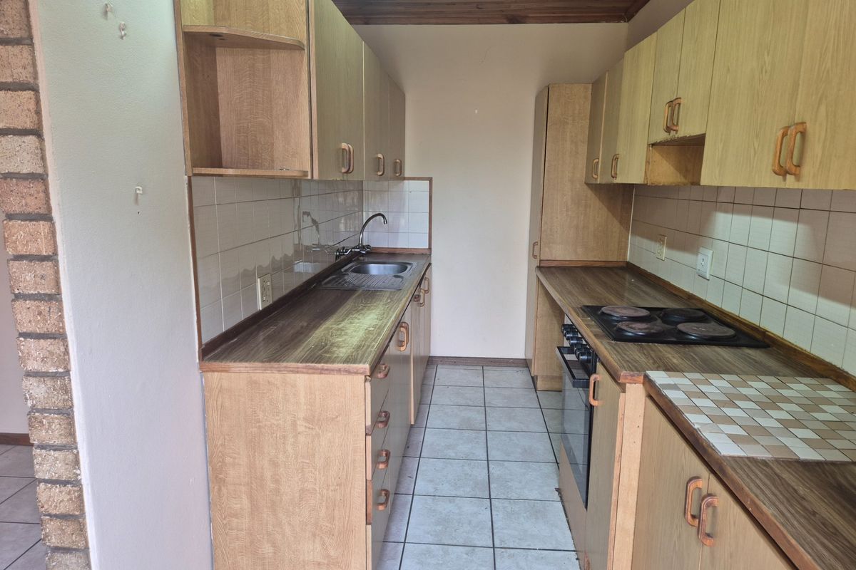 A dated galley-style kitchen featuring laminate cabinetry, built-in oven and hob, tiled backsplash, and tiled flooring, offering a functional layout ready for modernization.