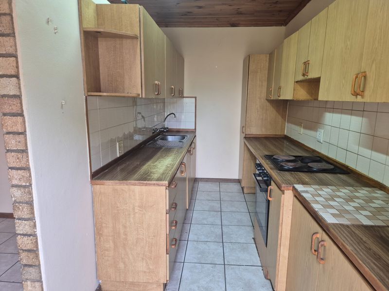 A dated galley-style kitchen featuring laminate cabinetry, built-in oven and hob, tiled backsplash, and tiled flooring, offering a functional layout ready for modernization.