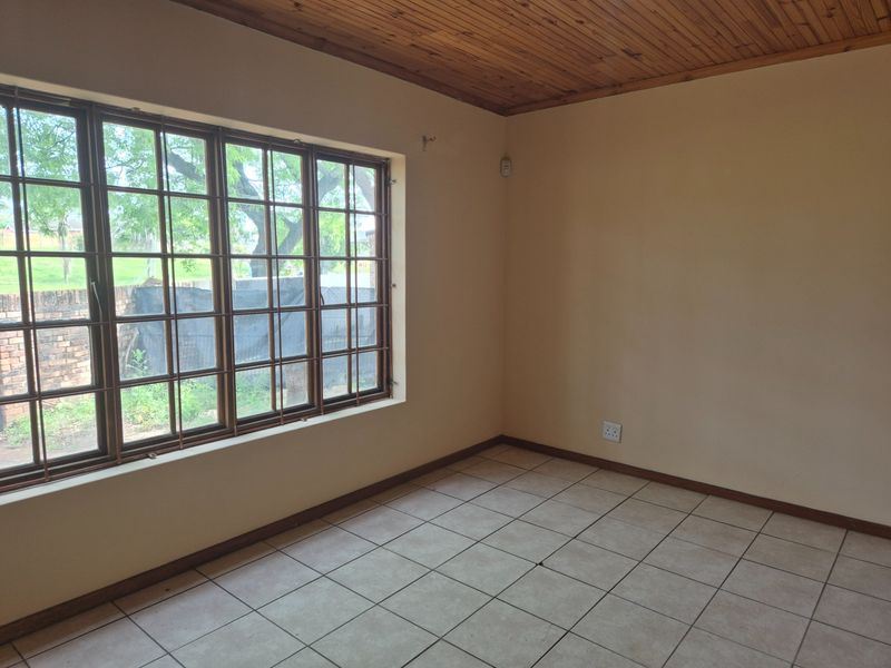 An empty living room featuring ceramic floor tiles, a timber tongue and groove ceiling, and a large window fitted with security bars.