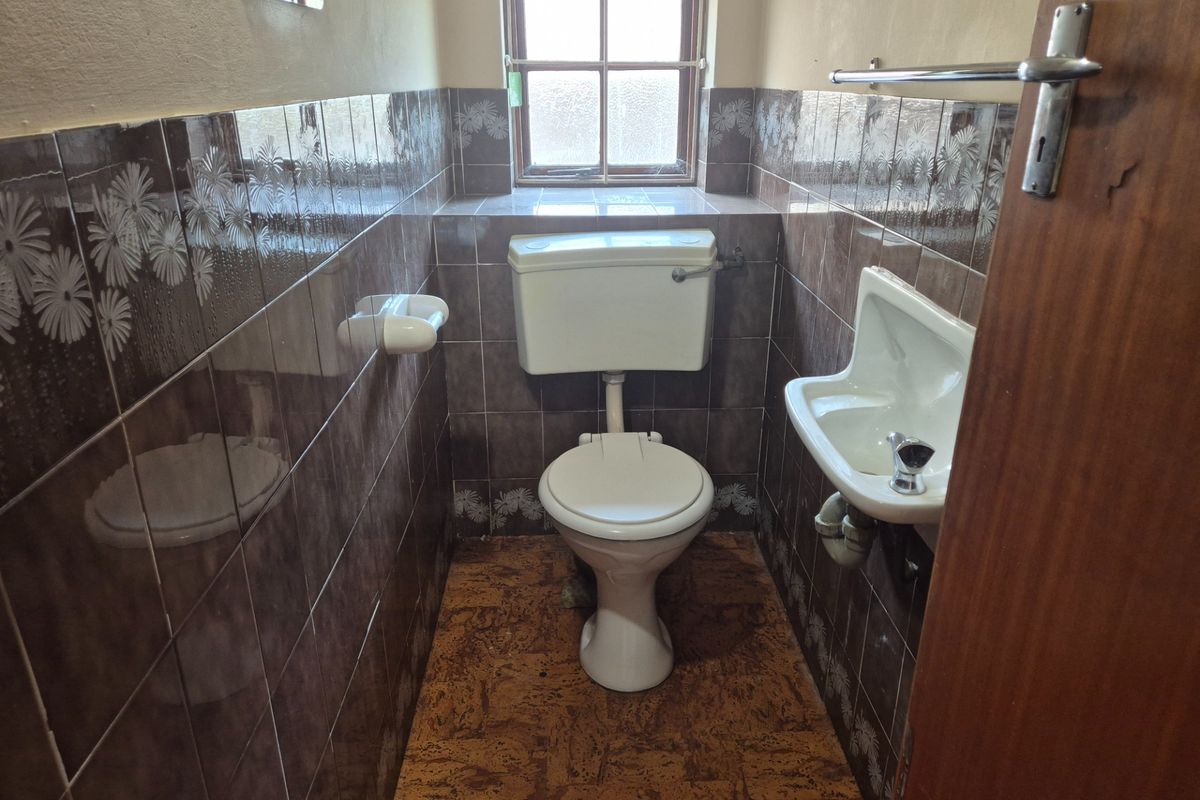 A compact guest bathroom featuring a toilet, wall-mounted basin, and dated tiled finishes, offering potential for a modern renovation.