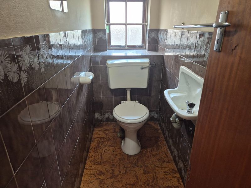 A compact guest bathroom featuring a toilet, wall-mounted basin, and dated tiled finishes, offering potential for a modern renovation.