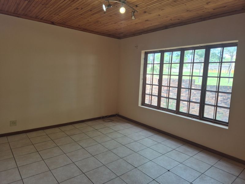 An empty living room featuring ceramic floor tiles, a wooden tongue and groove ceiling, and a large window with security bars.