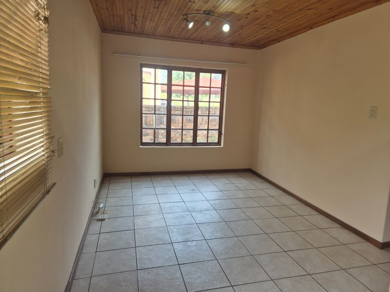 An empty bedroom featuring tiled flooring, a timber ceiling, and a window with security bars, offering a blank canvas for personalization.