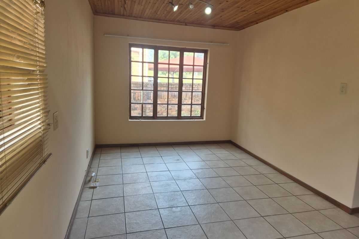 An empty bedroom featuring tiled flooring, a timber ceiling, and a window with security bars, offering a blank canvas for personalization.