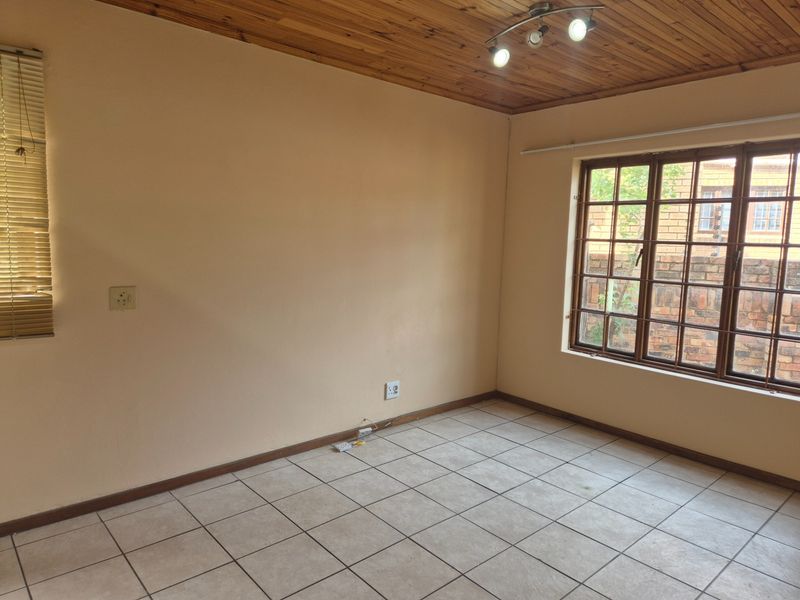 An empty bedroom featuring tiled flooring, a timber ceiling, and large windows with security bars, offering a blank canvas for personalization.