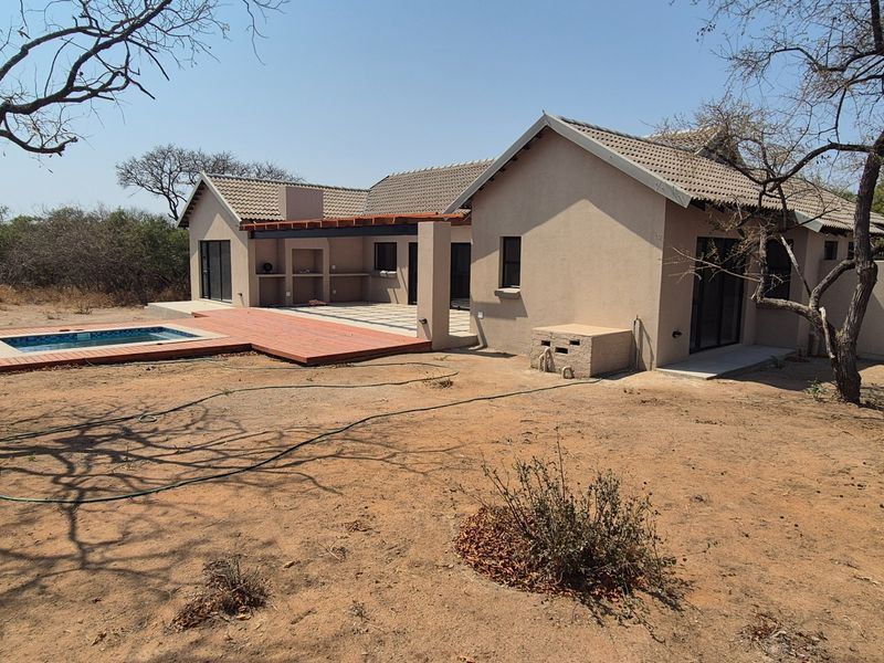 Rear view of the house featuring a swimming pool, wooden decking, and a covered patio with a built-in braai area.