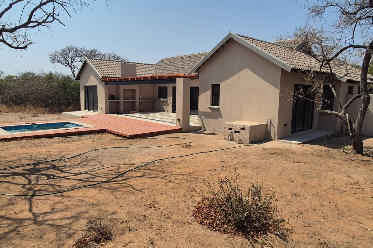 Rear view of the house featuring a swimming pool, wooden decking, and a covered patio with a built-in braai area.