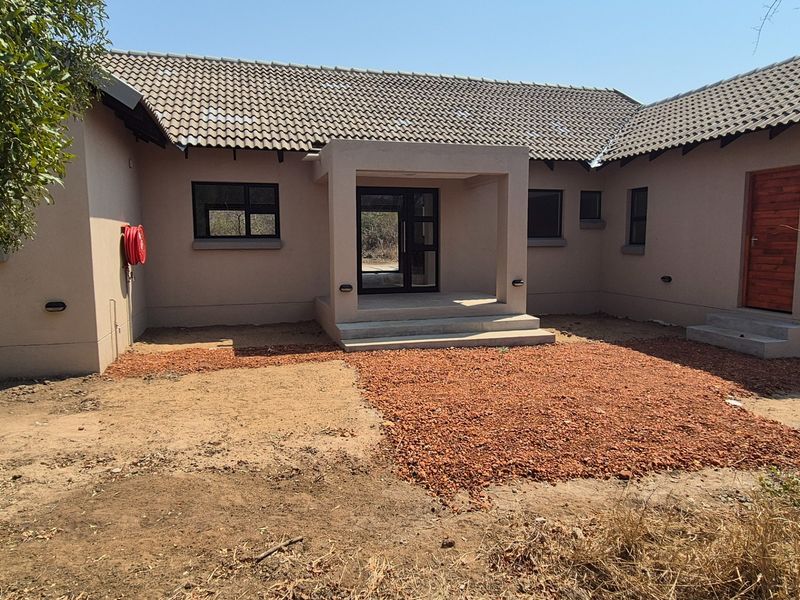 Rear exterior view of a house featuring a tiled roof, covered entrance with concrete steps, and unfinished landscaping area.
