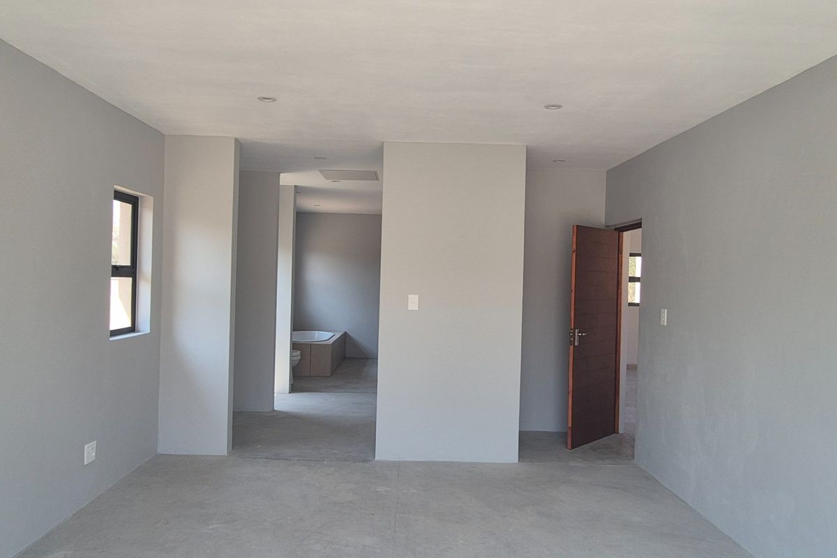 An empty, neutral-toned bedroom featuring recessed lighting and an adjoining en-suite bathroom area, providing a clean canvas for interior design.