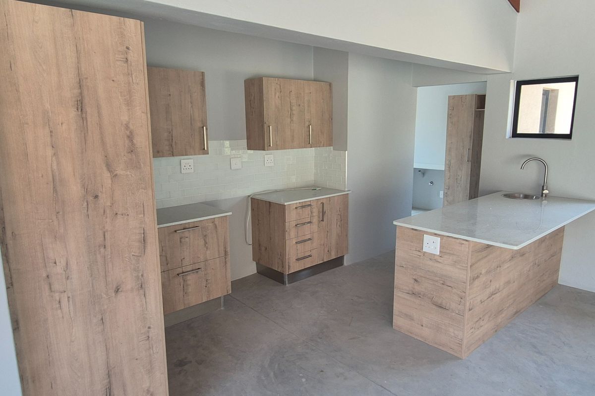 A modern, empty kitchen featuring wood-look cabinetry, stone countertops, a central island with a sink, and a clean subway tile backsplash.