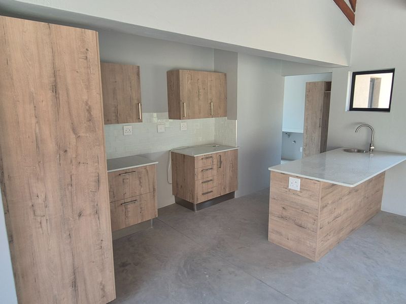 A modern, empty kitchen featuring wood-look cabinetry, stone countertops, a central island with a sink, and a clean subway tile backsplash.