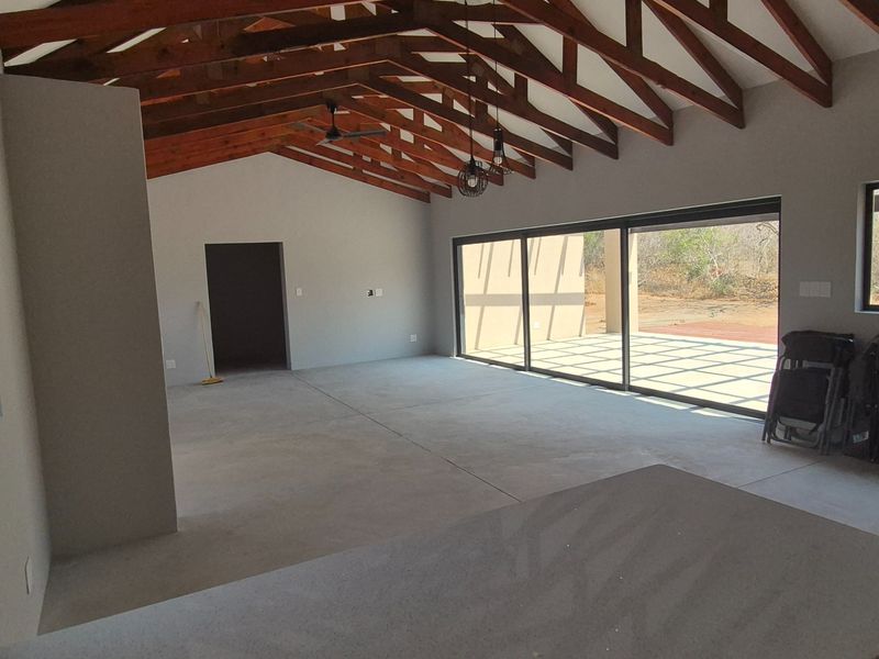 Spacious open-plan living area featuring high exposed timber trusses, polished concrete floors, and large sliding doors opening to an outdoor patio.