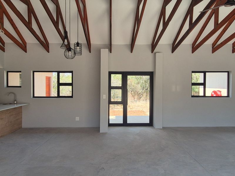 Spacious open-plan living area featuring exposed timber roof trusses, polished concrete floors, and modern aluminium fixtures with direct access to the outdoors.