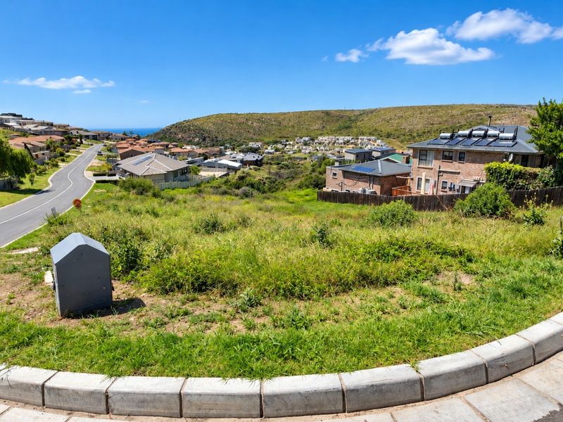 A vacant residential plot featuring concrete kerbing and a utility connection box, situated in a developed neighbourhood with surrounding residential properties.