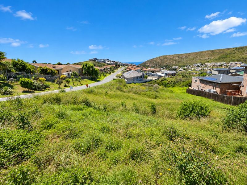 An elevated view overlooking a vacant residential plot with surrounding neighborhood houses and distant coastal landscape.