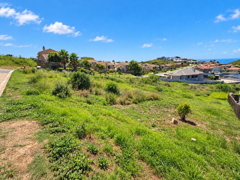 A vacant residential plot featuring a sloped landscape with views of the surrounding neighborhood and distant coastal scenery.