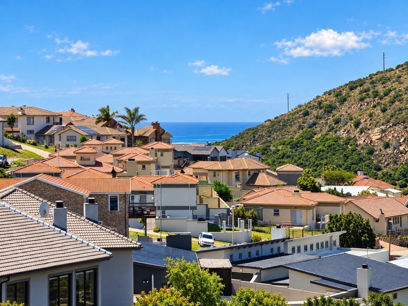 An elevated view overlooking a residential neighborhood with terracotta-tiled roofs, set against a backdrop of rolling hills and the distant ocean.
