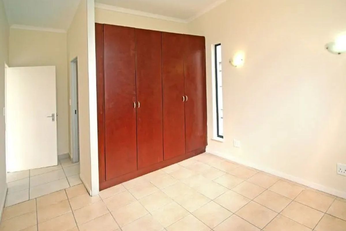 A bright, empty bedroom featuring neutral tiled flooring and floor-to-ceiling built-in wooden cupboards.