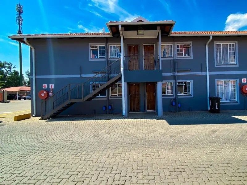 Exterior view of a multi-story apartment building featuring a paved driveway, external staircase, and secure entrance doors.