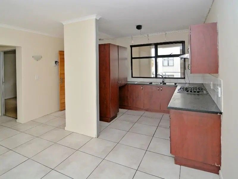 A functional kitchen featuring dark wood cabinetry, a gas hob, extractor fan, and tiled flooring, offering a clean and practical layout.