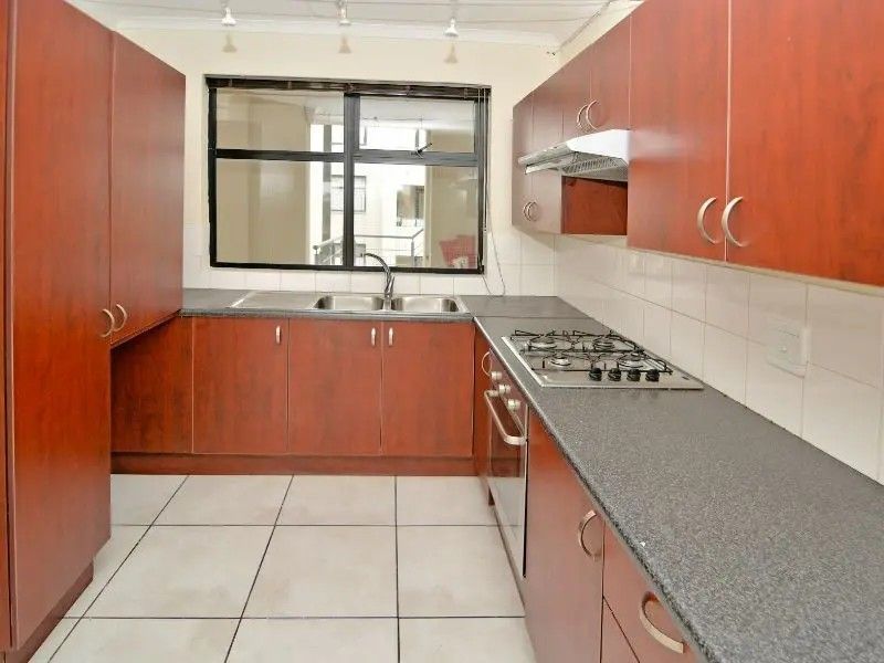 A functional kitchen featuring wood-finish cabinetry, dark laminate countertops, a gas hob, built-in oven, and tiled flooring with a neutral backsplash.