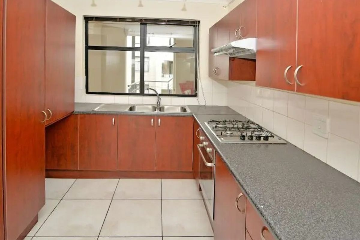 A functional kitchen featuring wood-finish cabinetry, dark laminate countertops, a gas hob, built-in oven, and tiled flooring with a neutral backsplash.