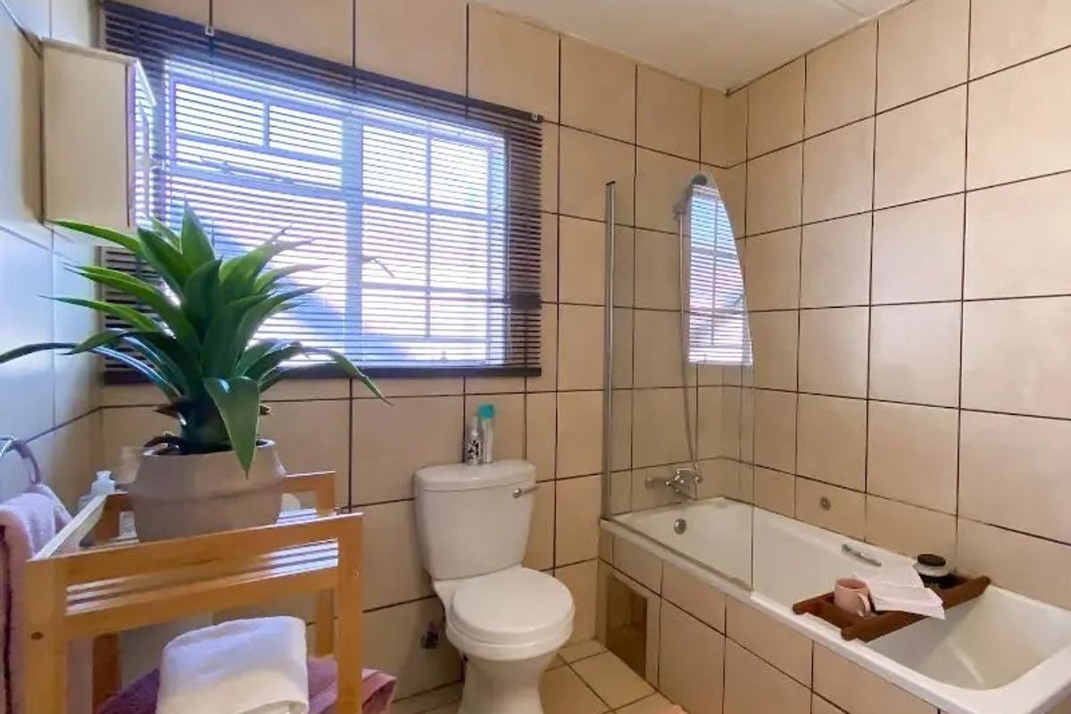 A functional bathroom featuring floor-to-ceiling wall tiles, a built-in bathtub with a glass shower screen, and a standard toilet.