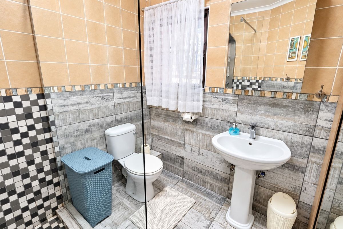 A functional bathroom featuring a pedestal sink, toilet, and a glass shower screen with mixed-pattern wall and floor tiling.