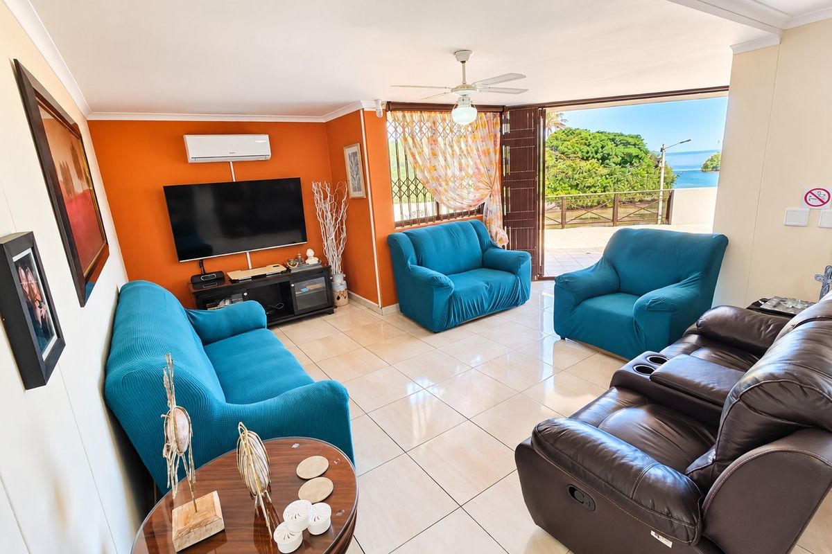 Spacious living room featuring tiled flooring, a ceiling fan, and split-system air conditioning, with direct access to a balcony offering scenic coastal views.