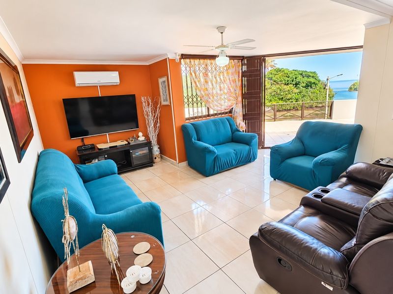 Spacious living room featuring tiled flooring, a ceiling fan, and split-system air conditioning, with direct access to a balcony offering scenic coastal views.