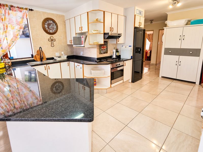 A functional kitchen featuring granite countertops, built-in cabinetry, a hob, oven, and extractor fan, with tiled flooring throughout.