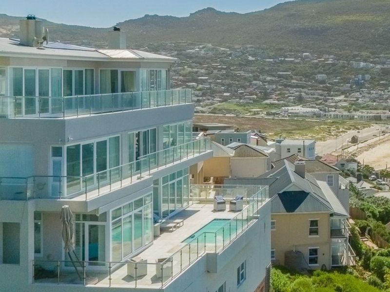 Aerial view of a modern multi-story coastal residence featuring expansive glass balconies, a private swimming pool, and panoramic views of the surrounding landscape.