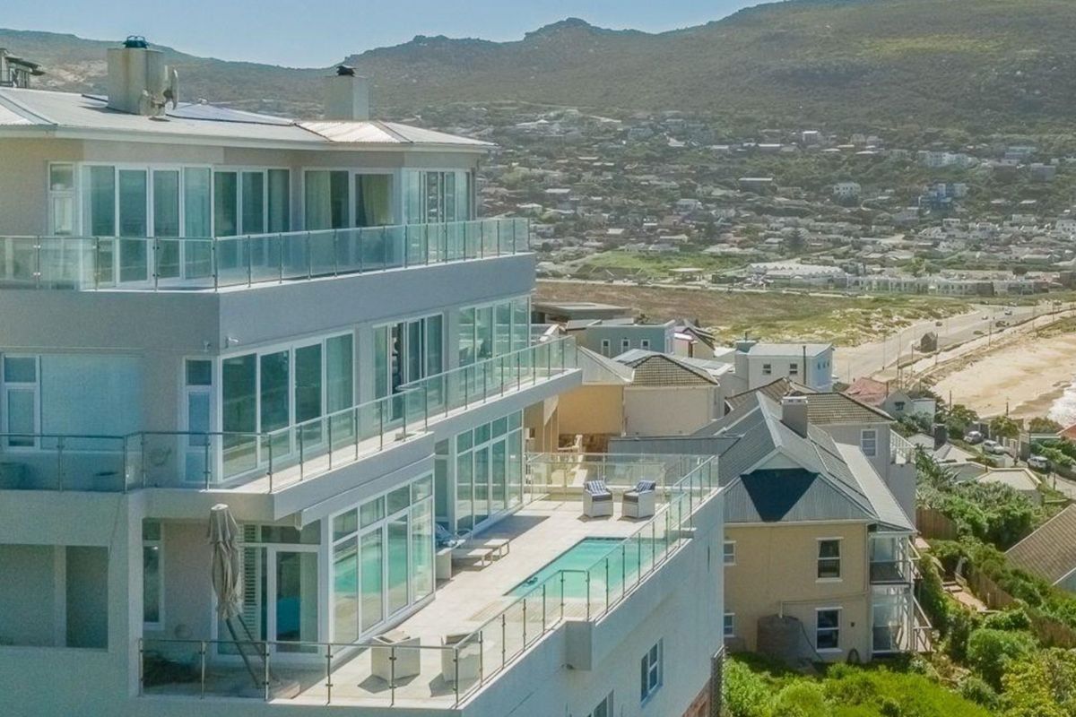 Aerial view of a modern multi-story coastal residence featuring expansive glass balconies, a private swimming pool, and panoramic views of the surrounding landscape.