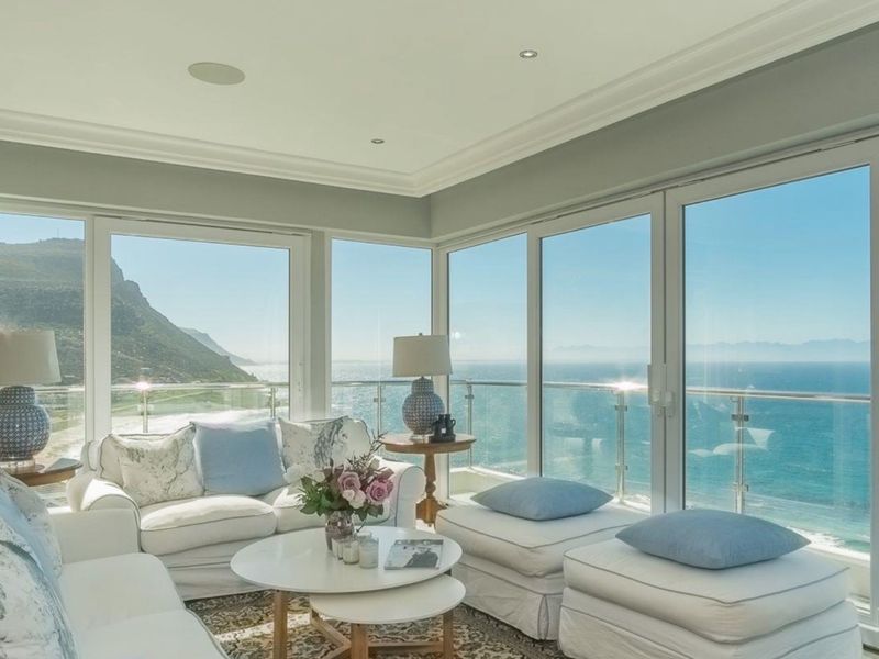 Bright living area featuring expansive floor-to-ceiling glass doors that offer panoramic ocean and mountain views, complemented by recessed lighting and elegant crown molding.