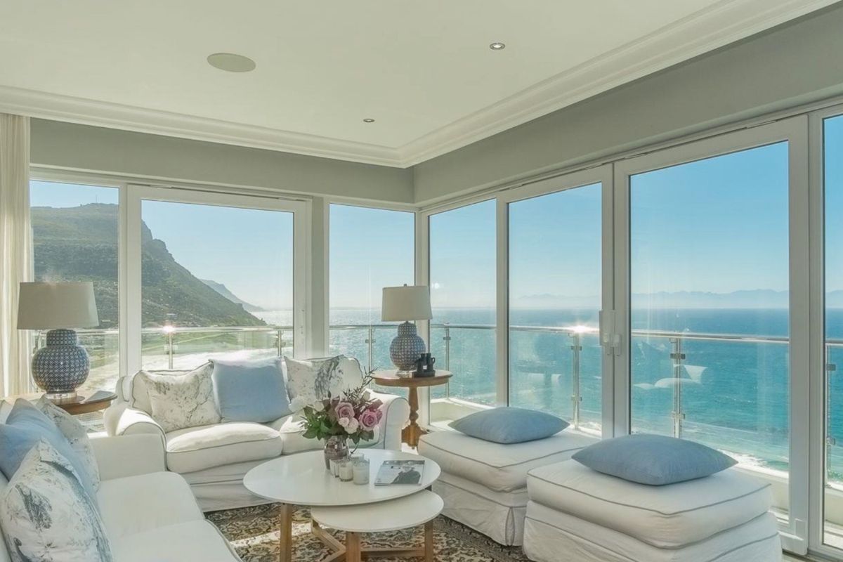 Bright living area featuring expansive floor-to-ceiling glass doors that offer panoramic ocean and mountain views, complemented by recessed lighting and elegant crown molding.