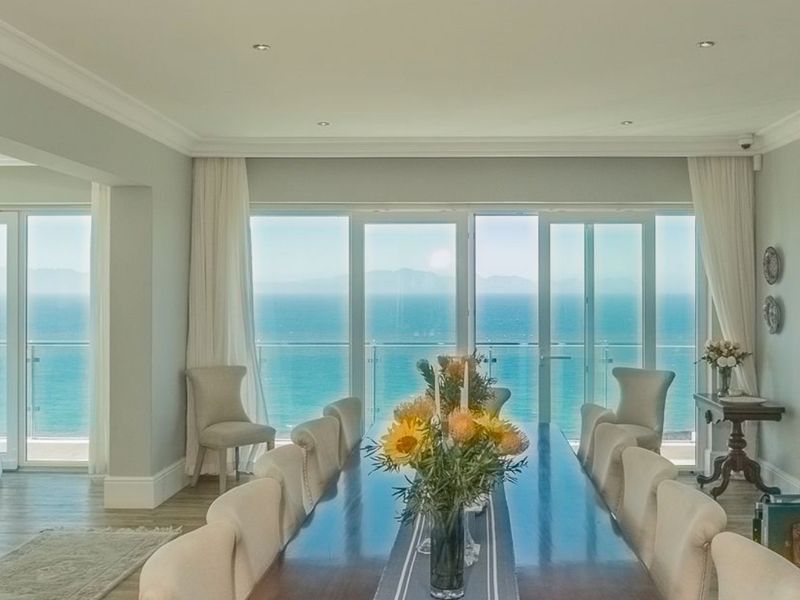 Elegant dining room featuring expansive glass sliding doors that open to a balcony with stunning, uninterrupted ocean views.