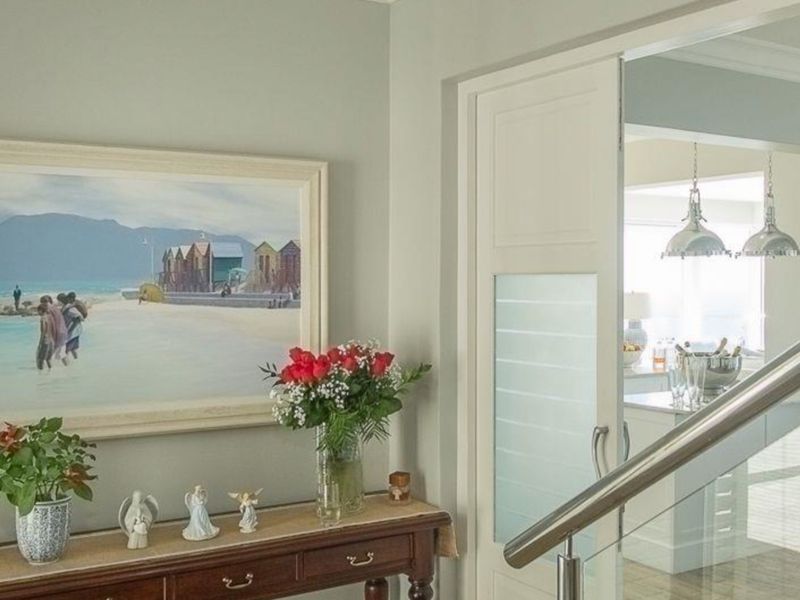 A bright hallway featuring a modern sliding door with frosted glass panels and a sleek stainless steel handrail leading to an adjacent living space.