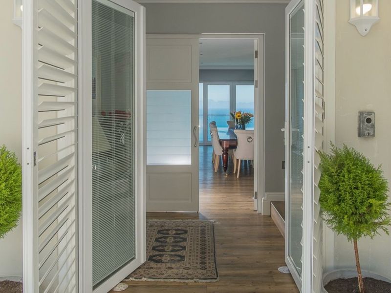 An inviting entrance hall featuring hardwood flooring and louvered shutters, providing a clear view through to the dining area and ocean beyond.