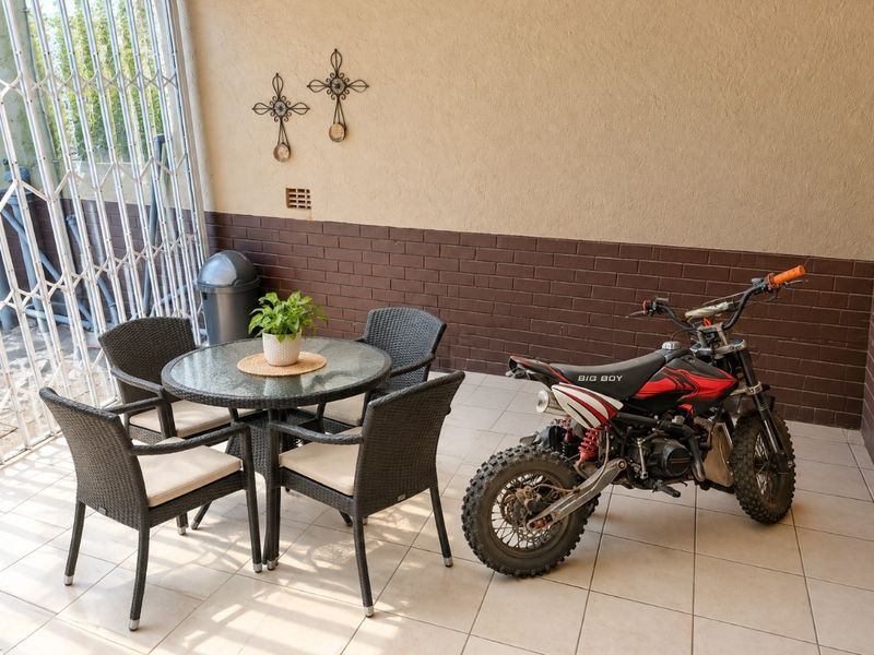 A covered patio area featuring tiled flooring, brick wall accents, and a secure metal gate, providing a functional outdoor space.