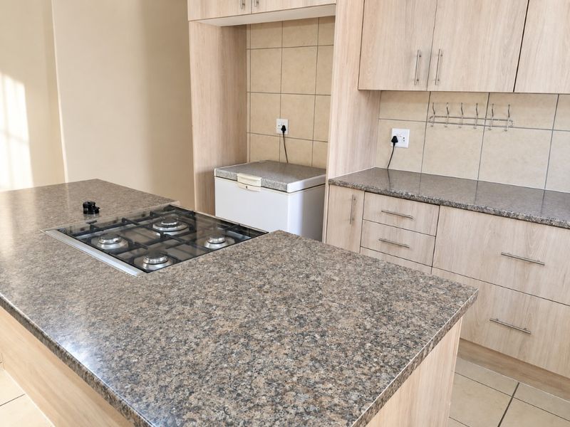 Modern kitchen featuring light wood cabinetry, granite-look laminate countertops, a central island with a built-in gas hob, and neutral tiled backsplash.