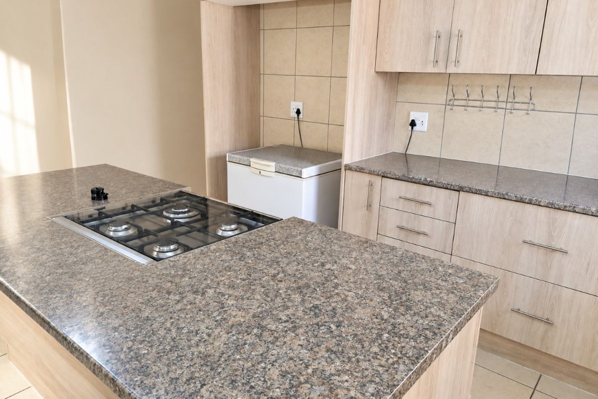 Modern kitchen featuring light wood cabinetry, granite-look laminate countertops, a central island with a built-in gas hob, and neutral tiled backsplash.