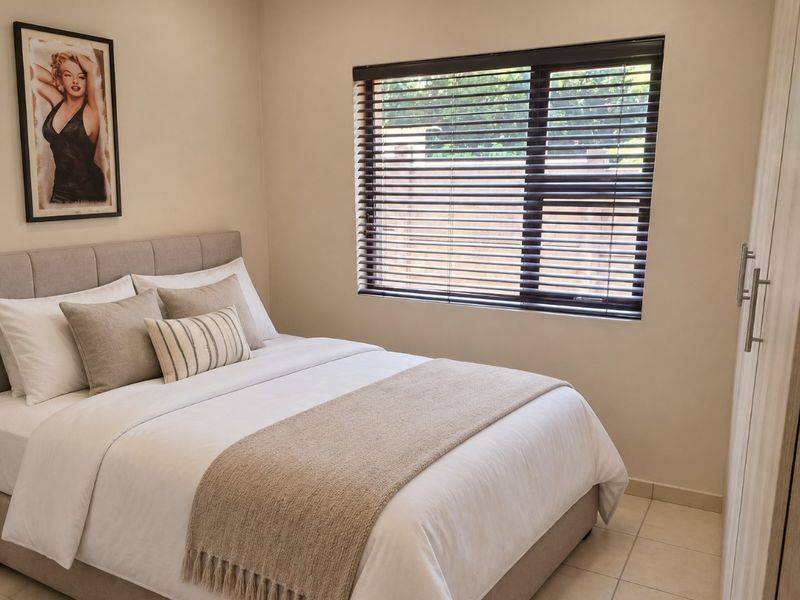 A well-maintained bedroom featuring neutral tones, tiled flooring, a built-in wardrobe, and venetian blinds for privacy.