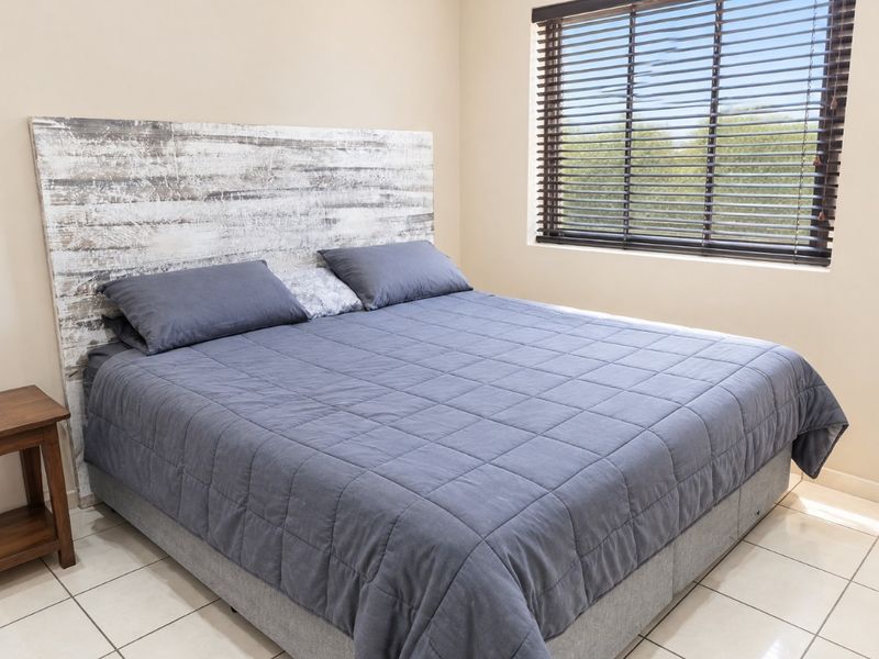 A well-maintained bedroom featuring neutral wall tones, tiled flooring, and fitted venetian blinds, providing a clean and functional living space.