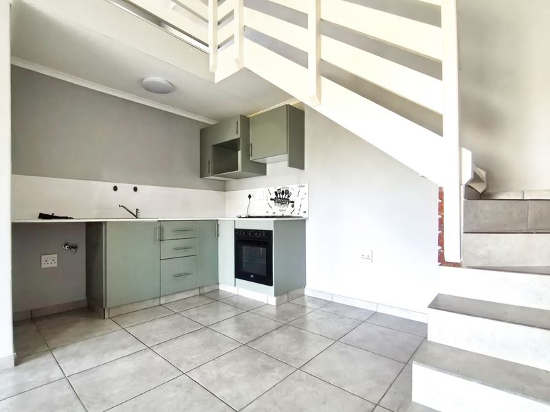 Compact kitchen featuring built-in cabinetry, oven, hob, and tiled flooring, situated conveniently beneath an internal staircase.