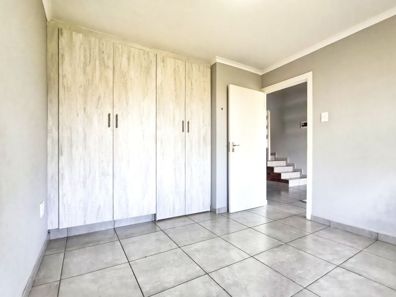A clean, empty bedroom featuring light-toned built-in cupboards and neutral tiled flooring, offering a versatile space ready for personalization.